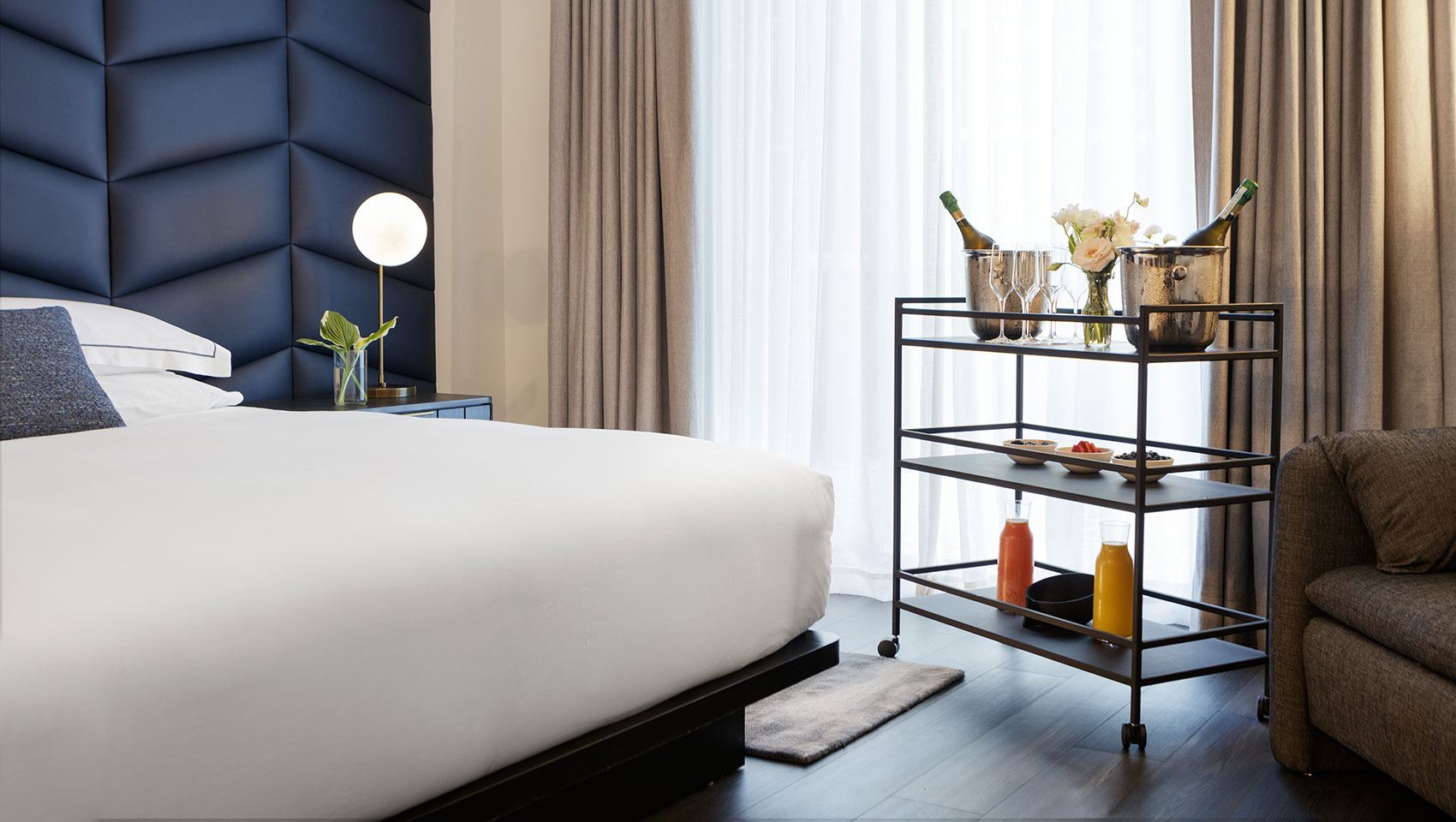 A hotel room with a king bed, a mimosa cart set up by the window